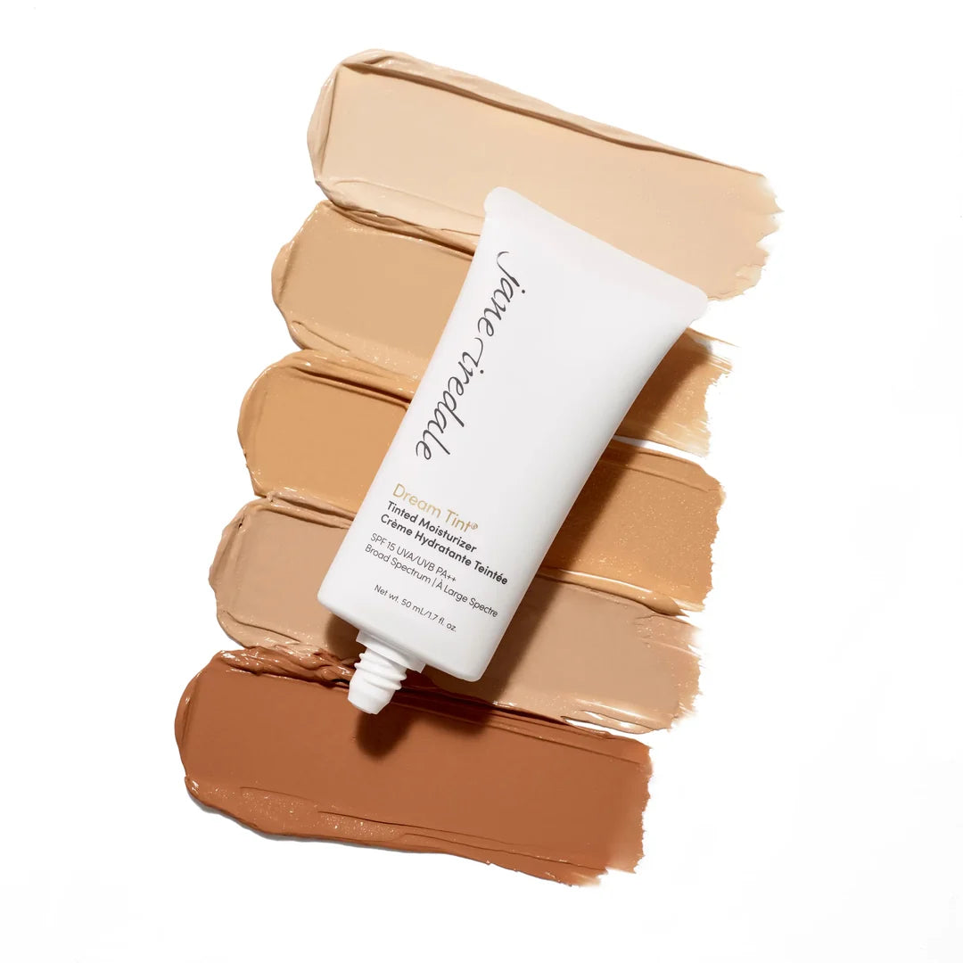 Uncapped jane iredale Dream Tint Tinted Moisturiser tube arranged diagonally over five foundation shade swatches.