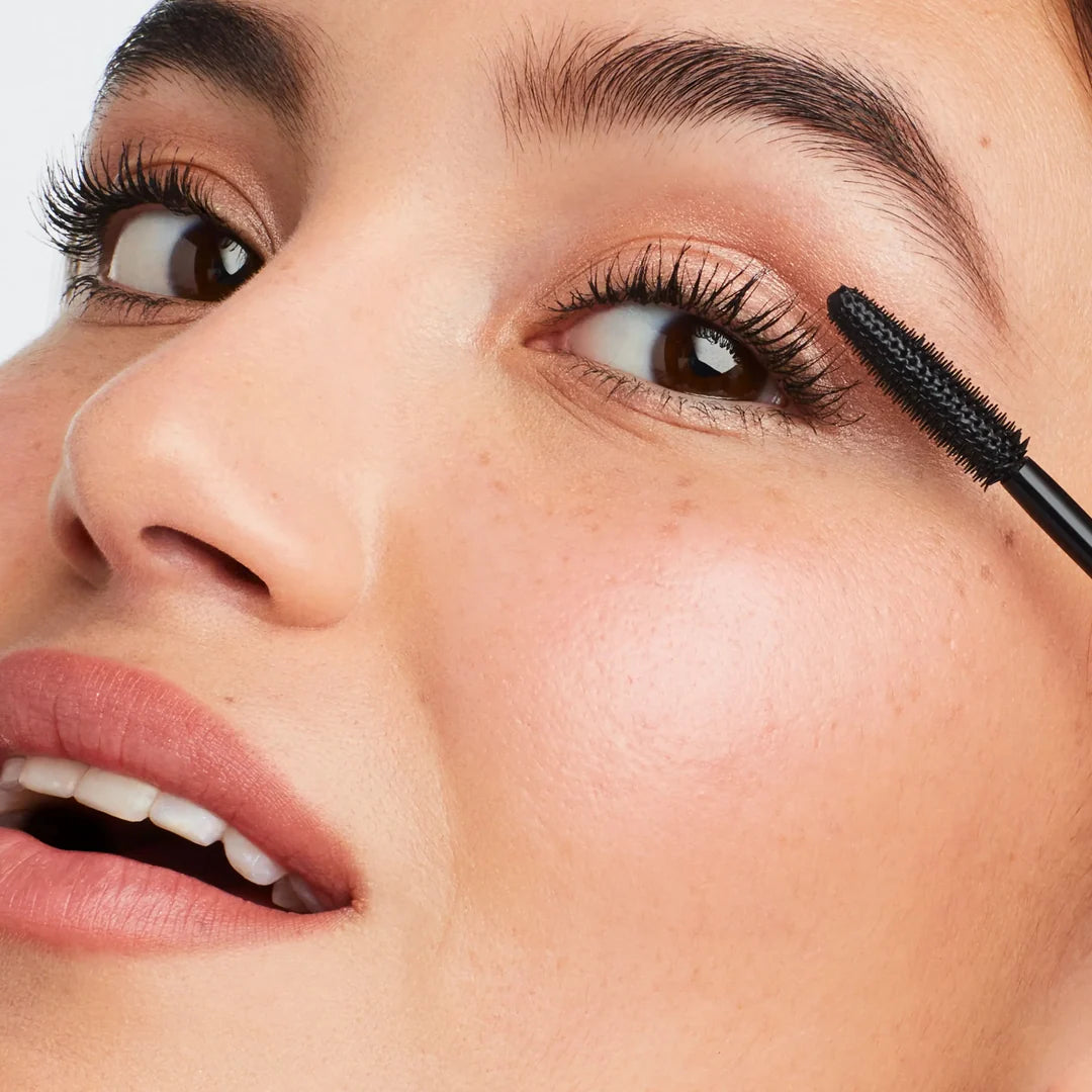 Model applying jane iredale Lash Fixation mascara to her upper lashes with a black mascara wand.