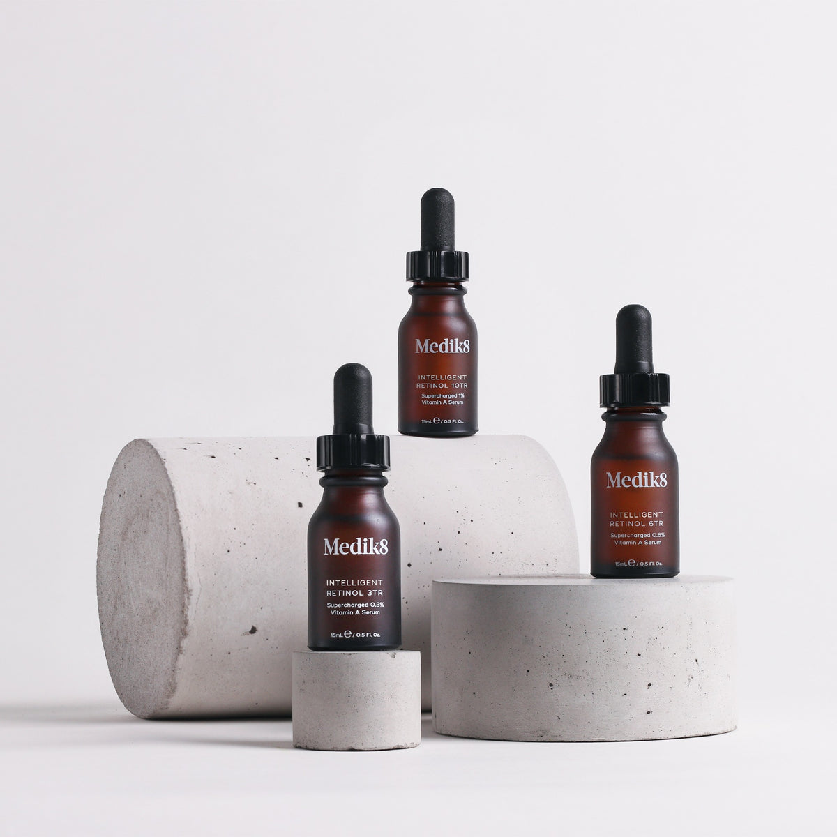 Three Medik8 skincare bottles on concrete stands against a light background